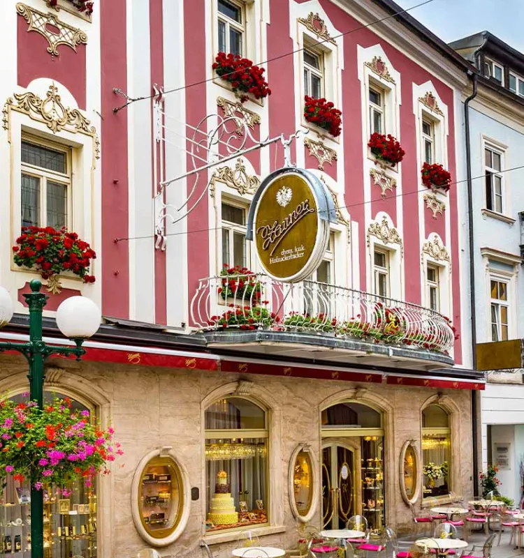 Historische Fassade der Konditorei Zauner in Bad Ischl mit roten Blumen und Außentischen.