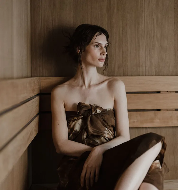 Woman relaxing in the sauna at the Grand Elisabeth, surrounded by warm wood and a tranquil atmosphere during a wellness vacation in Bad Ischl.