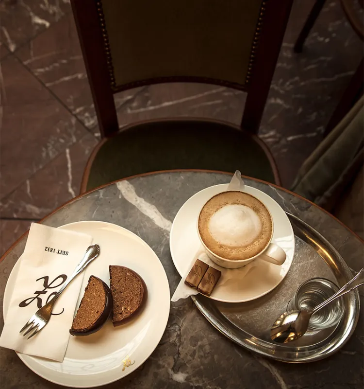 Cappuccino with water and chocolate cake on a marble table at Konditorei Zauner.