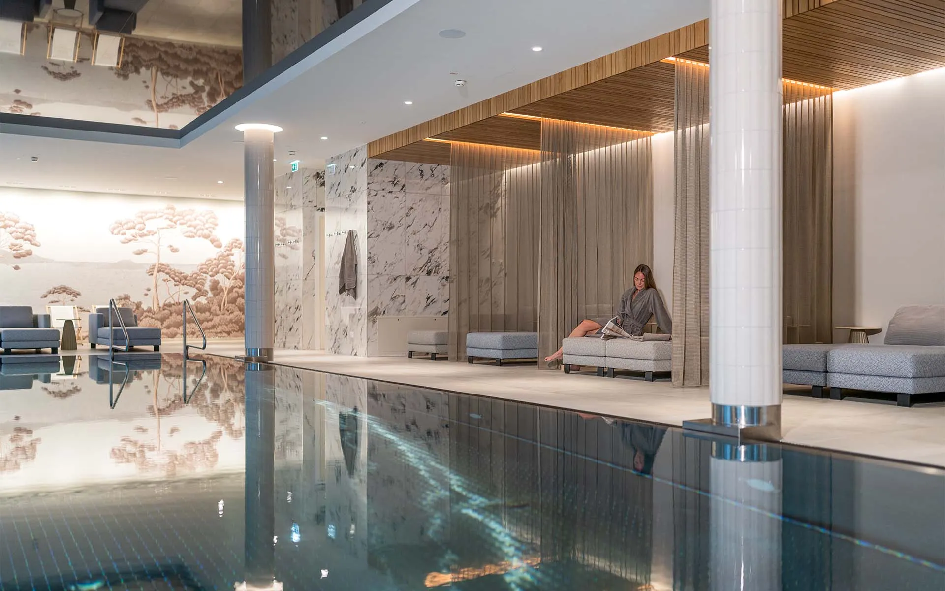 Frau im Bademantel entspannt im Wellnessbereich im Grand Elisabeth Hotel mit Liegen, Vorhängen und Marmorwänden