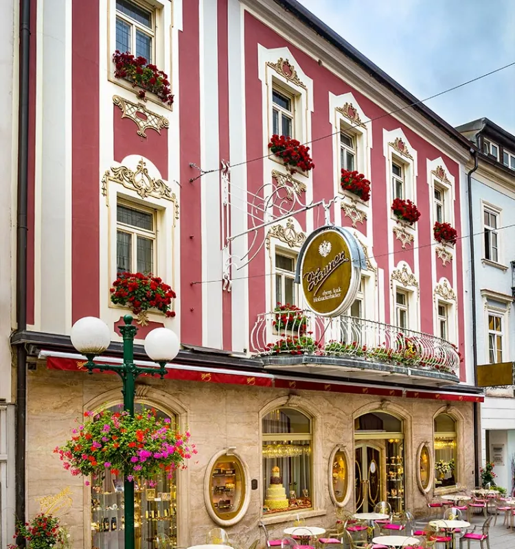 Historische rot-weiß gestreifte Fassade der Konditorei Zauner in Bad Ischl mit Blumenschmuck und Gastgarten