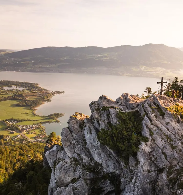 Blick vom Gipfel des Almkogels mit Gipfelkreuz über See und Berglandschaft im Abendlicht