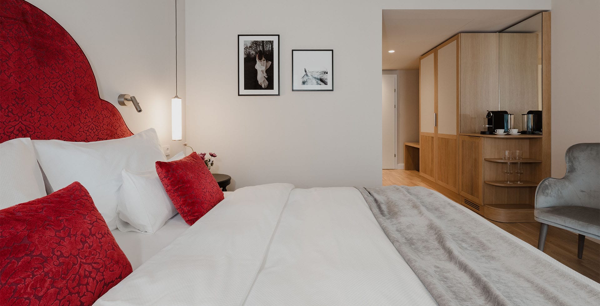 Zimmeransicht im Hotel Bad Ischl mit rotem Bett, Holzmöbeln und Espressomaschine