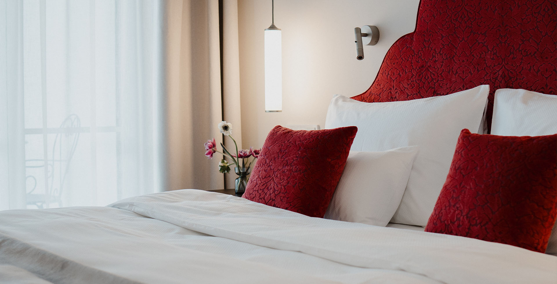 Detailaufnahme vom Bett im Hotel Bad Ischl mit rotem Kopfteil und floraler Deko