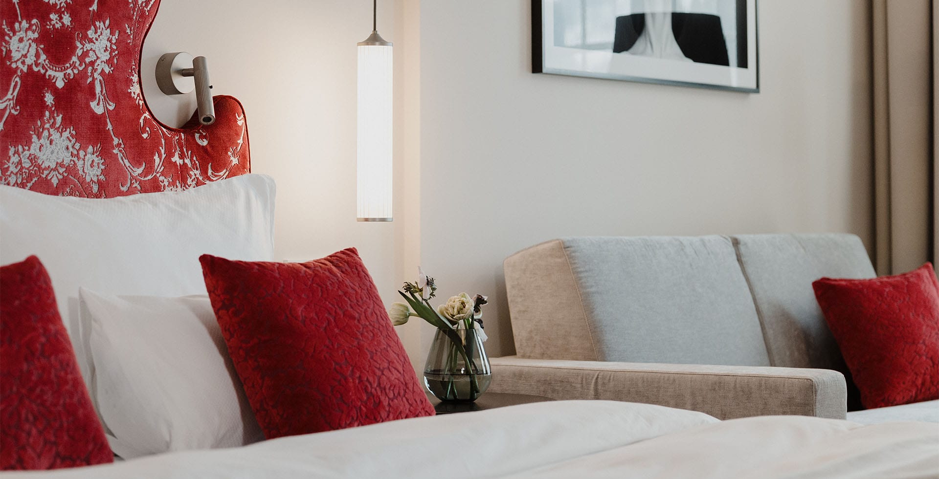 Rote Kissen auf Bett und grauem Sofa im Designhotel in der Kaiserstadt mit stilvollem Kunstwerk im Hintergrund